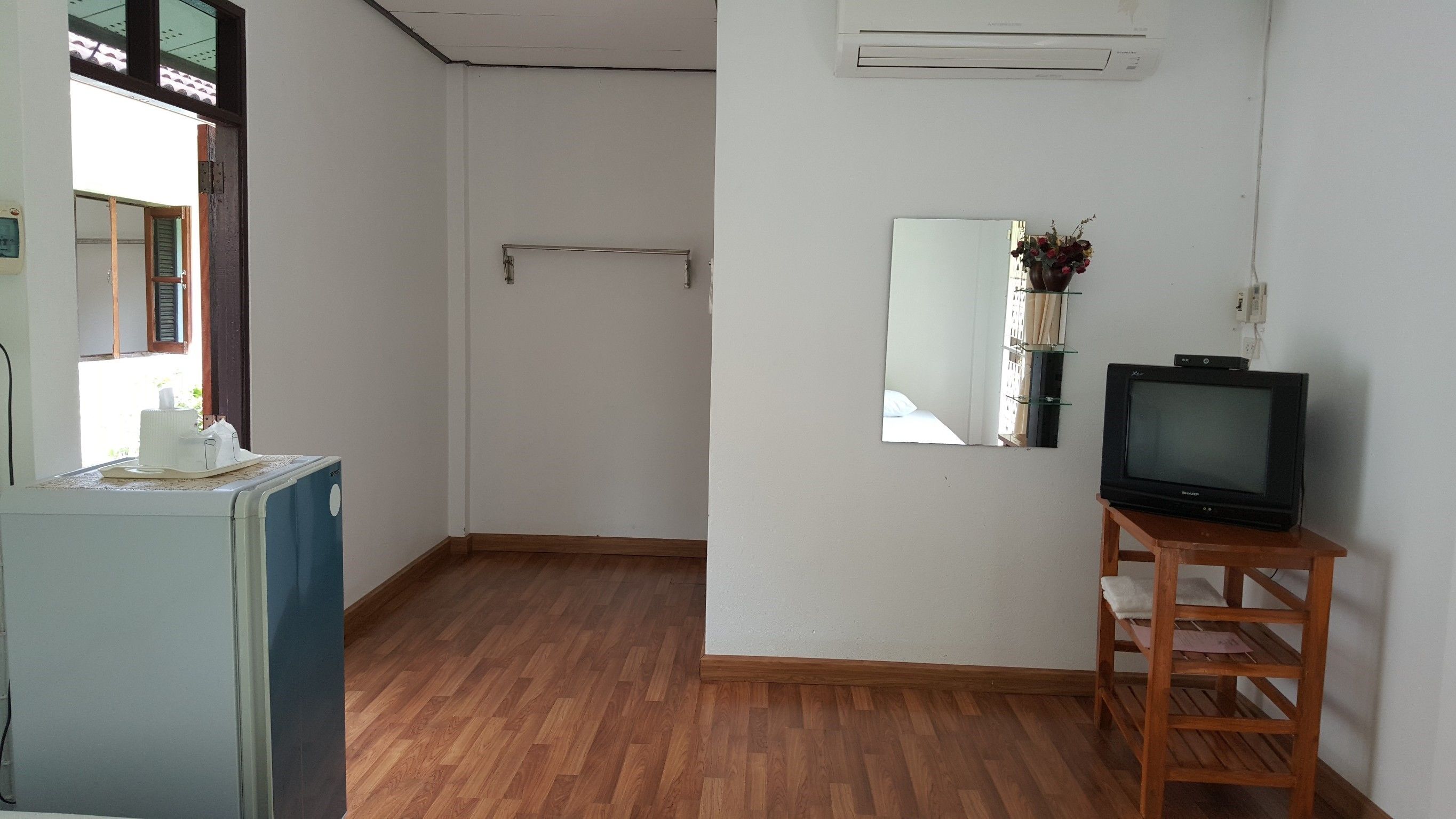 Een kamer met houten vloer, een wasmachine, een televisie op een houten standaard, een spiegel en een airconditioning.