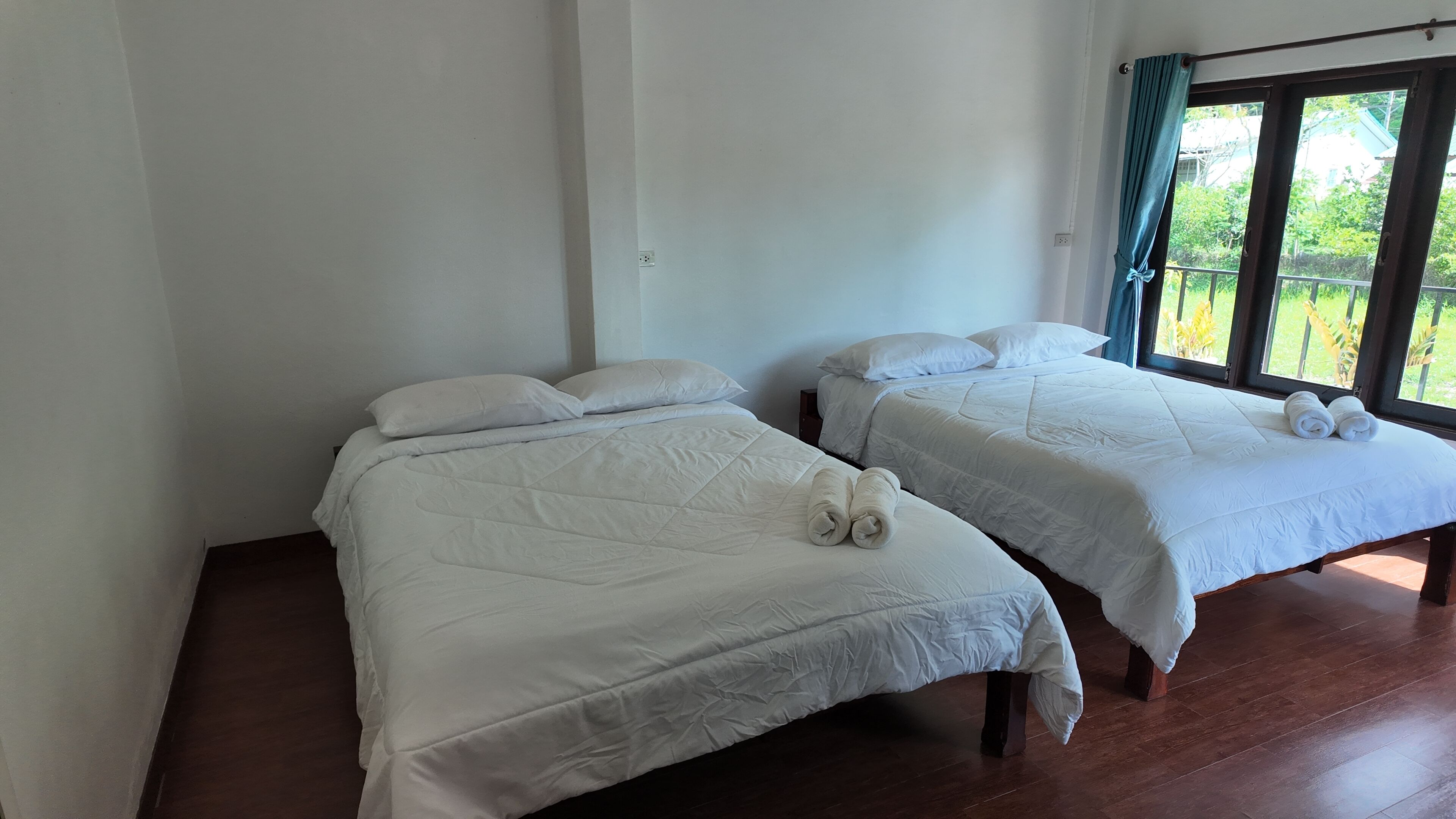 Dos camas individuales con ropa de cama y almohadas blancas, suelo de madera y una ventana con cortinas.