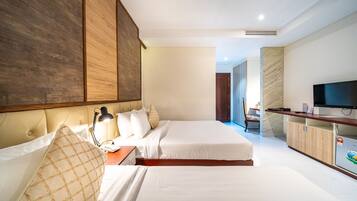 A modern hotel room with a large bed, a desk with a lamp, a TV, and a minibar.