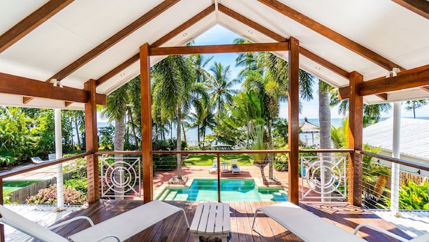 A covered outdoor area with wooden beams, a pool, and lounge chairs. - Beach House Cairns (Holloways Beach)