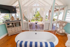 Quarto com uma banheira grande, um armário de madeira e vista para um deck e palmeiras.