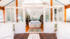 A spacious room with a wooden floor, a large window with sheer curtains, and a white bathtub with blue stripes. - Beach House Cairns (Holloways Beach)