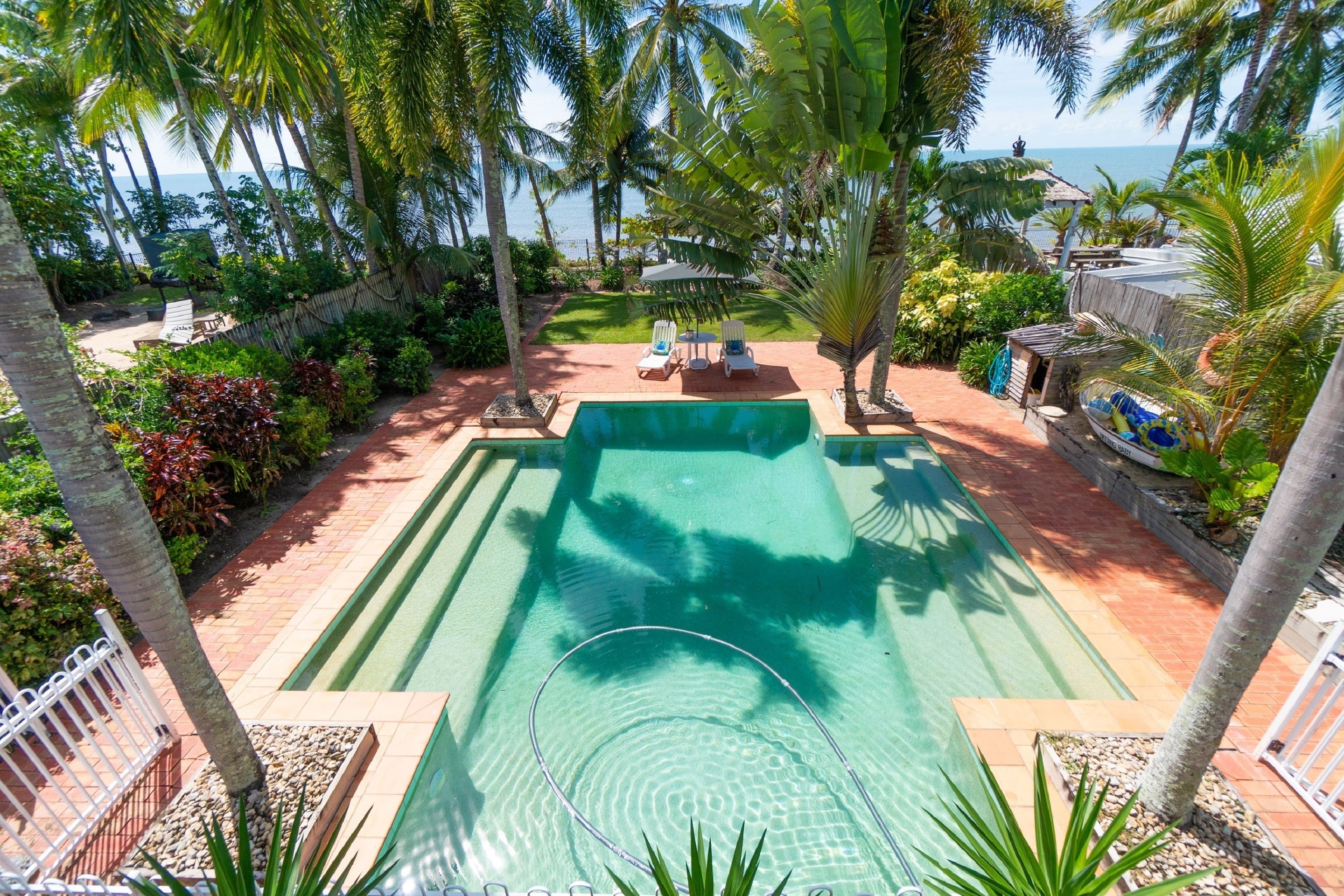 Una piscina con vista sull'oceano, circondata da palme e da una zona relax con lettini.