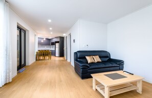 Un salon moderne avec un canapé en cuir noir, une table basse en bois et un coin repas comprenant une table et des chaises en bois.