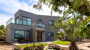 Une maison moderne à deux étages, dotée d’un balcon, d’une porte d’entrée et d’un petit jardin agrémenté d’un banc et d’un arbre.