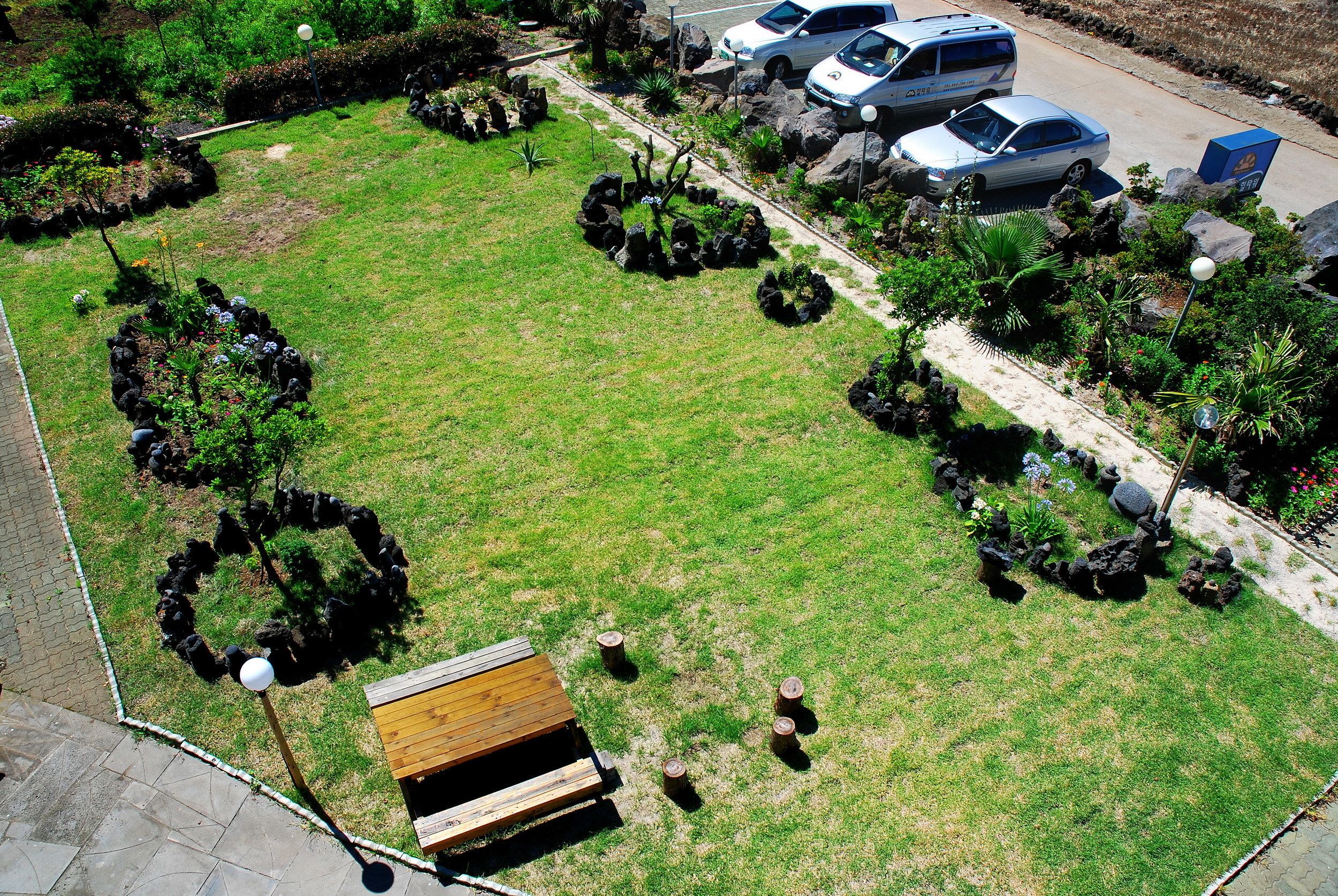 An aerial view of a landscaped garden with a wooden bench, a paved walkway, and parked cars.