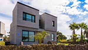 Un bâtiment moderne à deux étages, avec un mur en pierre à l’avant, de grandes fenêtres et un ciel dégagé.