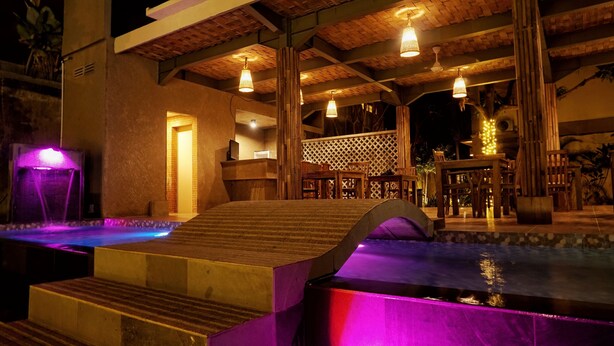 An outdoor pool area with a wooden deck, a water feature, and a seating area with tables and chairs. - The Inn by Sunsethouse (Senggigi)