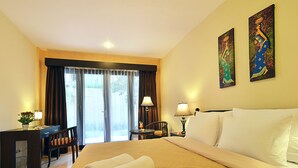 A hotel room with a bed, a desk, a chair, a lamp, and two paintings on the wall. - The Inn by Sunsethouse (Senggigi)