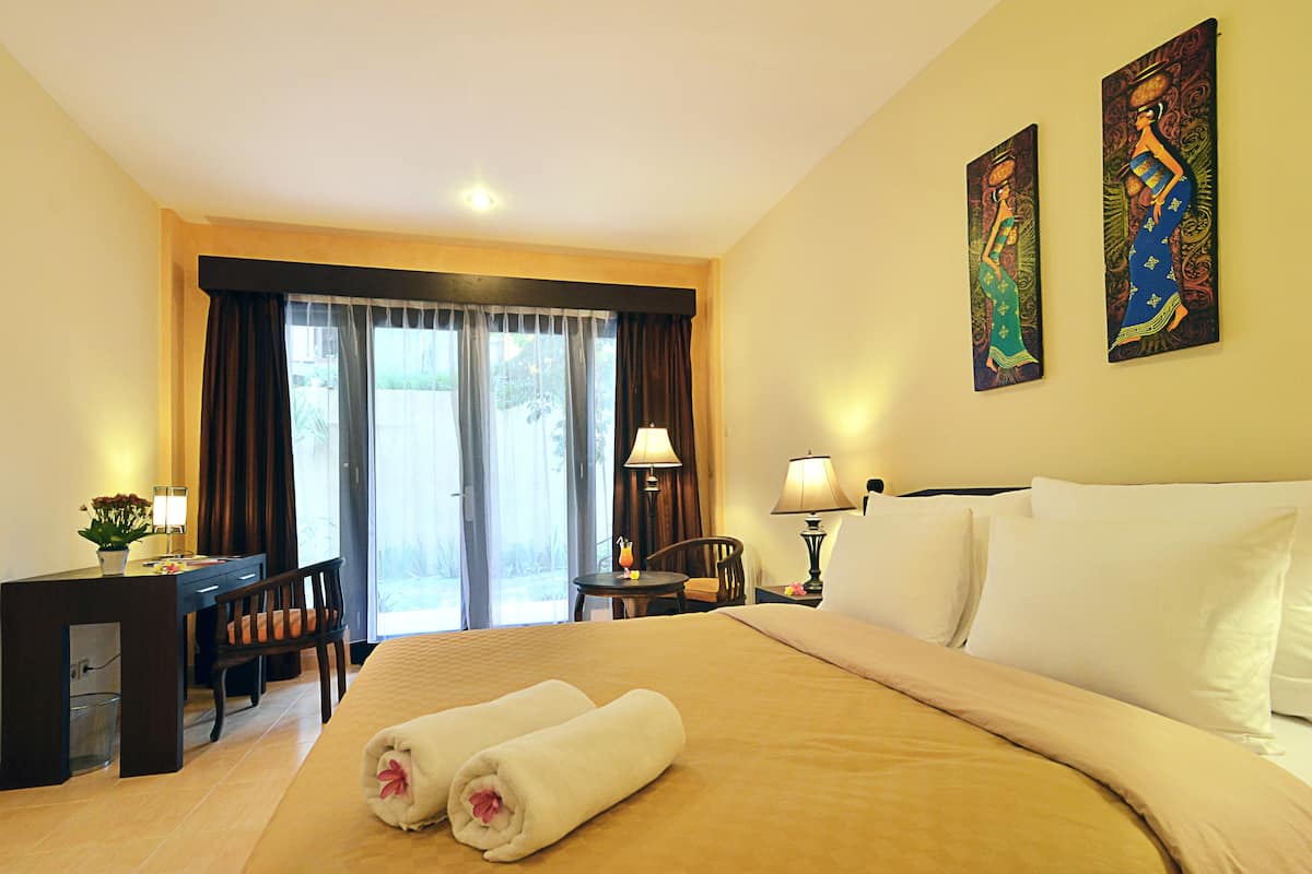 A hotel room with a bed, a desk, a chair, a lamp, and two paintings on the wall.