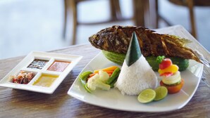 A plate with grilled fish, rice, vegetables, and lime slices. - The Inn by Sunsethouse (Senggigi)