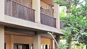 A person carrying a tray with a drink and a flower, standing in front of a building with a bamboo fence and a tree. - The Inn by Sunsethouse (Senggigi)