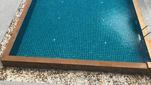 A rectangular swimming pool with a tiled surface, surrounded by a pebble border, and adjacent to a red and white fence. - Samui City Hotel (Koh Samui)