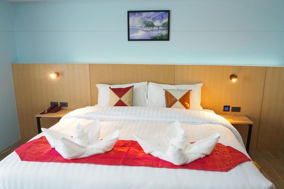 A neatly made bed with a red and white bedspread, two white pillows, and a framed painting above it.