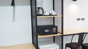 A compact room with a wooden desk, a black chair, a white mini-fridge, a coffee maker, and a shelf with a kettle and cups. - Samui City Hotel (Koh Samui)