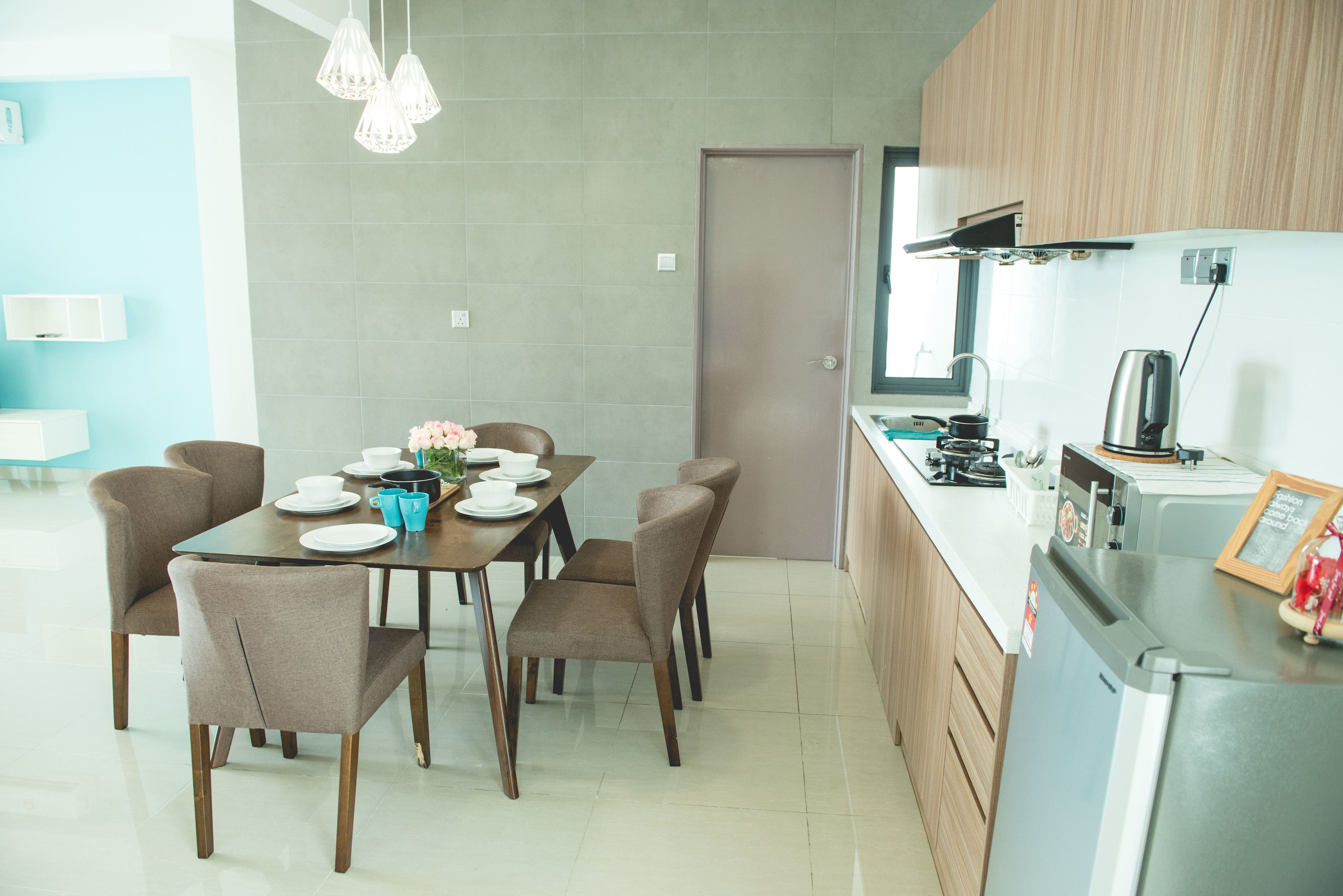 A modern kitchen with a dining area, featuring a stainless steel refrigerator, wooden cabinets, and a tiled backsplash.