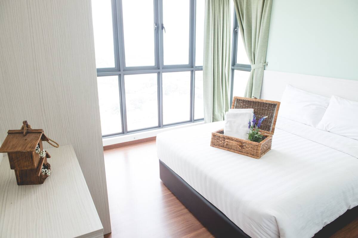 A neatly made bed with white linens, a wicker basket with flowers, and a wooden birdhouse on a white nightstand.