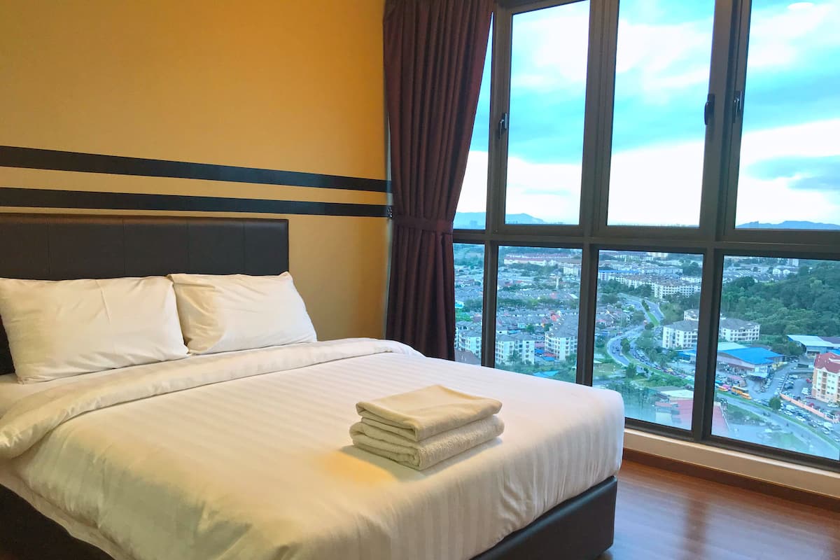 A hotel room with a large bed, a view of a cityscape through a window, and a curtain on the window.