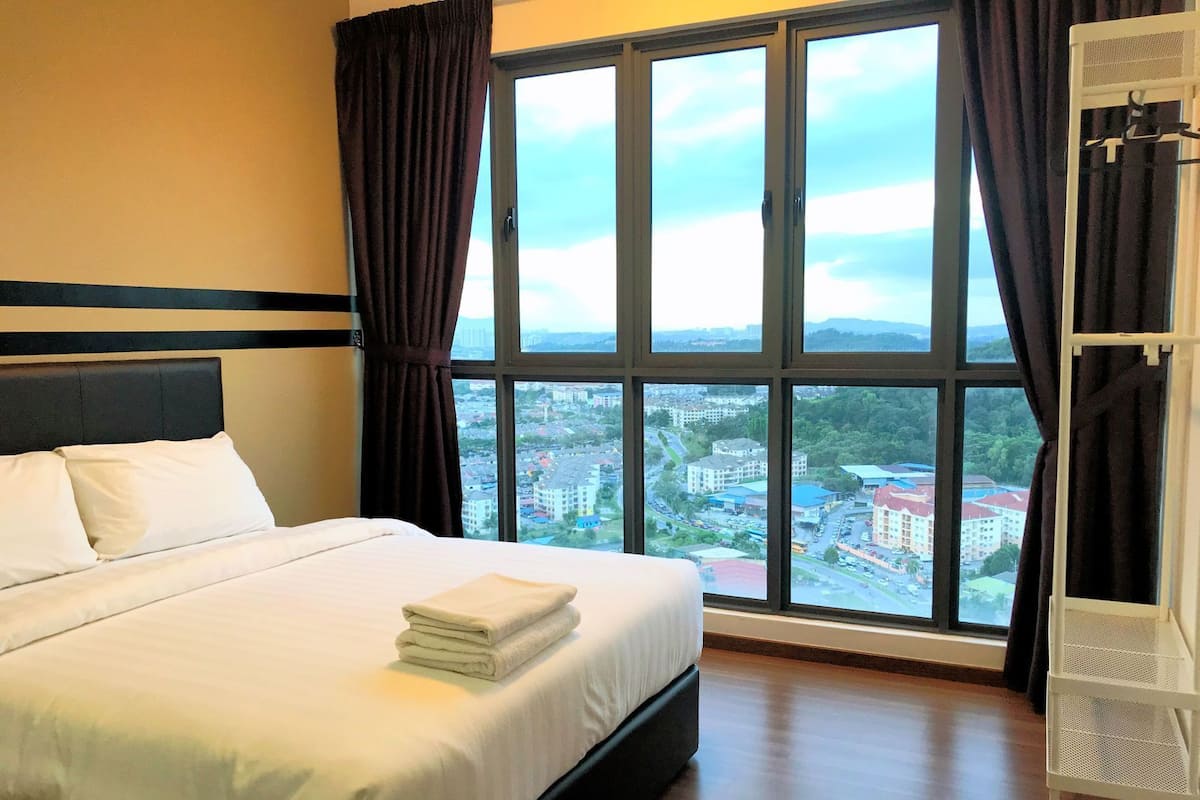 A hotel room with a bed, large windows, and a view of a cityscape.