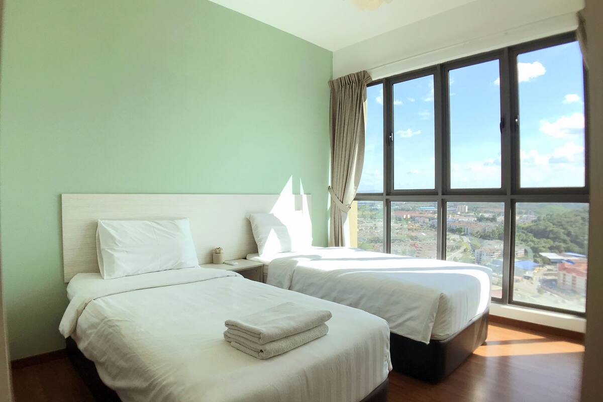 A hotel room with two beds, a large window with a city view, and a curtain.