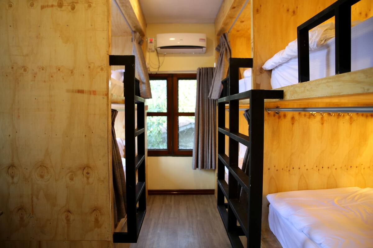 Un intérieur en bois avec des lits superposés, une fenêtre avec des rideaux et un appareil de climatisation.