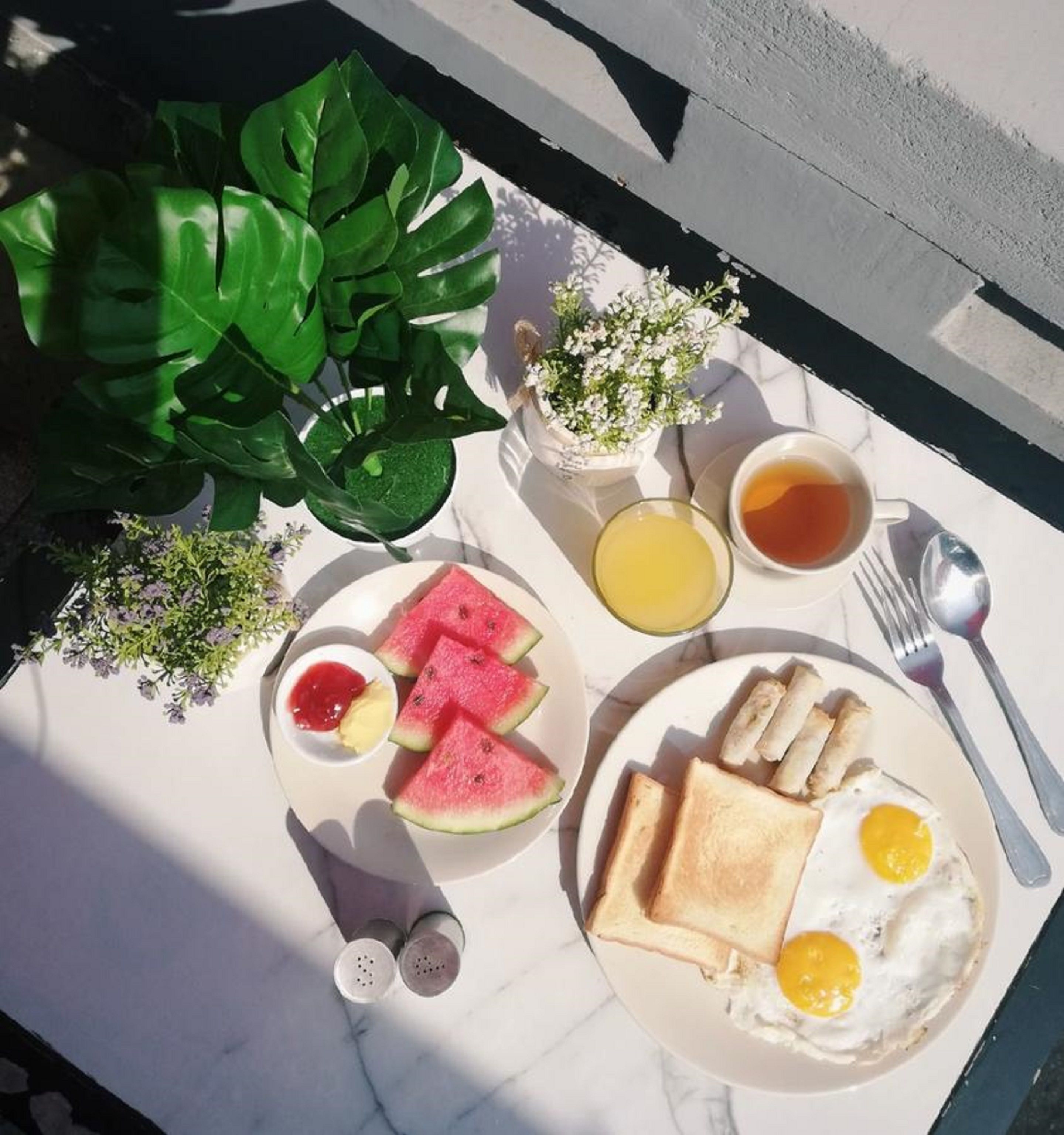 A breakfast tray with toast, eggs, watermelon, and tea on a marble table outdoors.