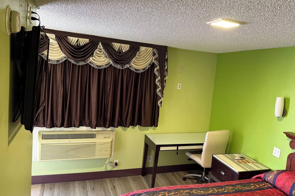 A room with a bed, a desk, an air conditioner, a chair, and a window with curtains.