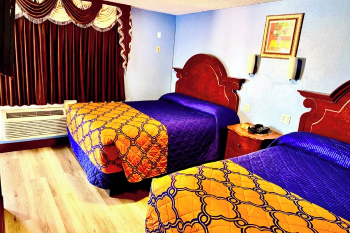 A hotel room with two beds, a red headboard, a wall-mounted picture, and a window with curtains.
