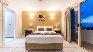 Een hotelkamer met een groot bed, twee nachtkastjes met lampen, een schilderij aan de muur en een stadszicht door een groot raam.