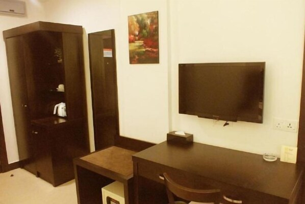 Habitación de hotel con un escritorio de madera oscura, un televisor de pantalla plana montado en la pared, una mesita de noche pequeña y una silla.
