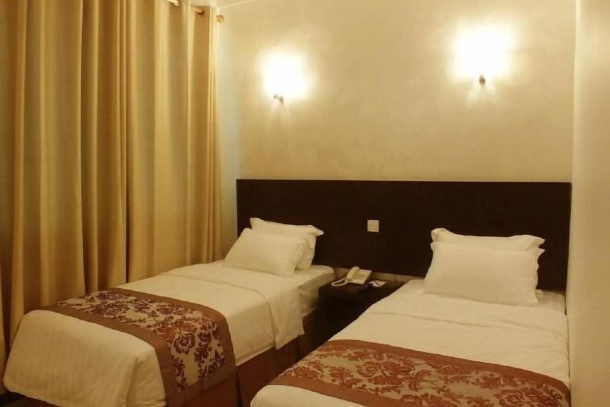 Una habitación de hotel con dos camas individuales, cada una con cabecera, mesitas de noche y lámparas.