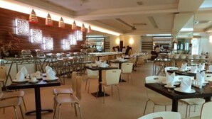 Um restaurante amplo, com várias mesas e cadeiras, algumas com guardanapos e pratos brancos.