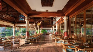 Un restaurant situé à l’intérieur, avec des tables et des chaises en bois, un plafond haut et de grandes fenêtres.