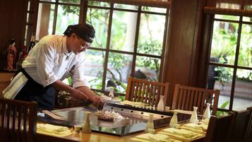 A chef preparing food at a wooden table with a view of greenery outside.