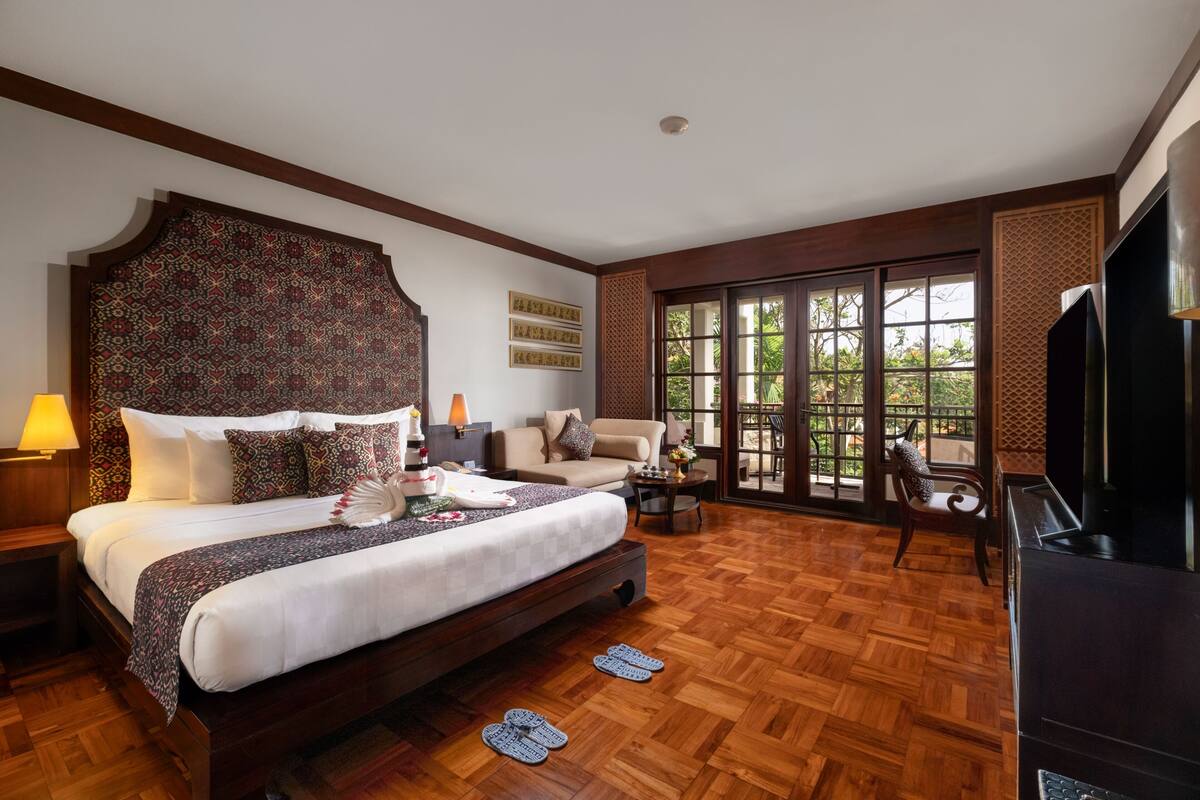 Une chambre spacieuse avec un grand lit, un canapé, une télévision et un balcon offrant une vue agréable.