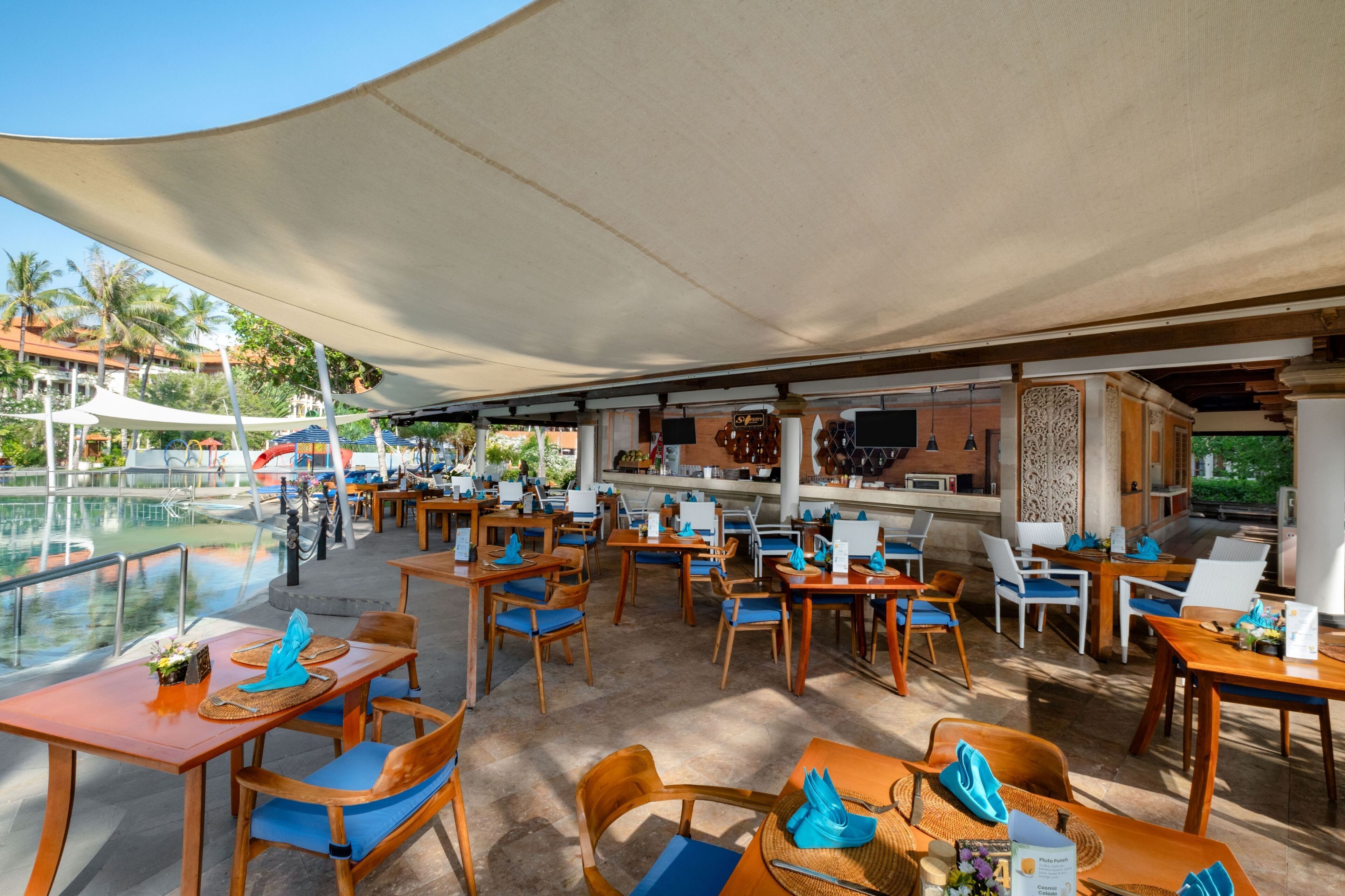 An outdoor dining area with tables and chairs, a pool, and a bar area.