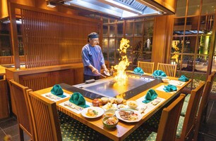 Ein Restaurant mit einem großen Tisch, Holzsesseln und einem Koch, der eine Feuershow aufführt.