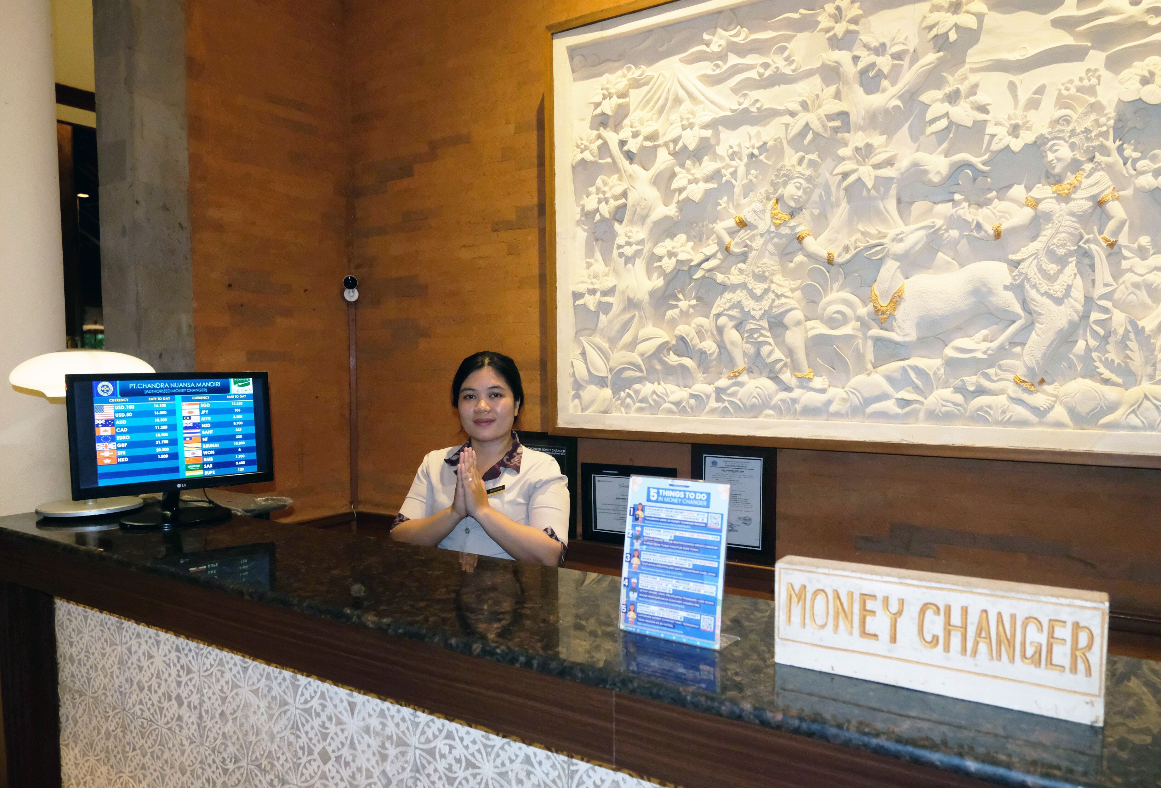 A reception desk with a computer monitor, a 'Money Changer' sign, and a large decorative wall.