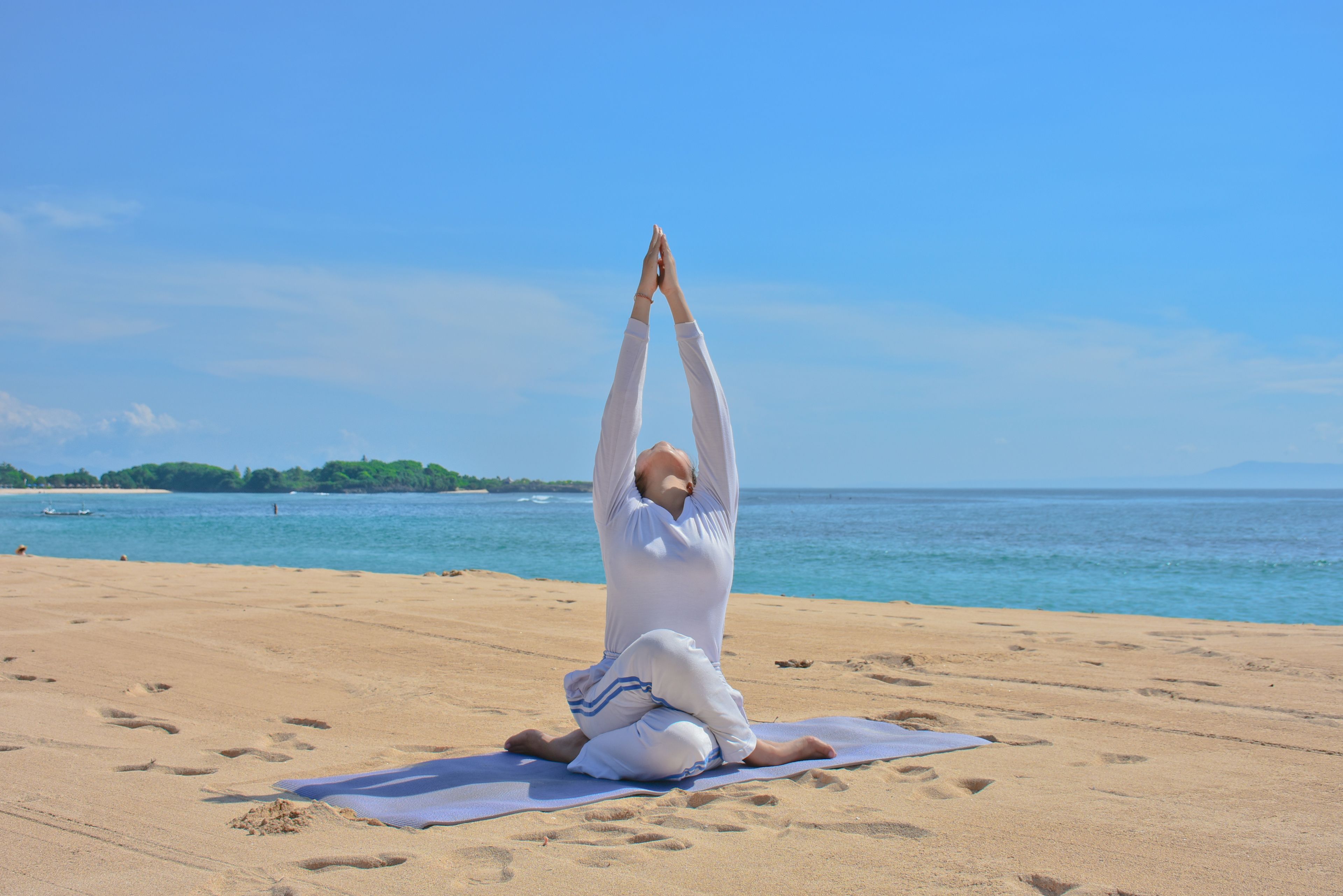 Iemand doet yoga op het strand, met een heldere lucht en een rustige zee op de achtergrond.