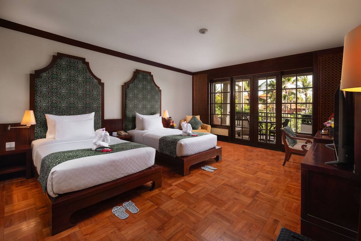 Une chambre d’hôtel avec deux lits, un plancher en bois, de grandes fenêtres et un téléviseur.