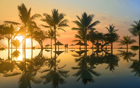 A serene beach scene with palm trees and a sunset.