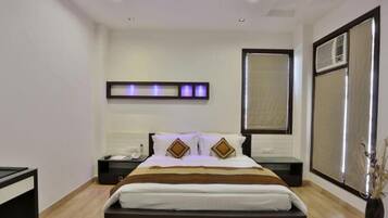 Una habitación de hotel moderna con una cama grande, mesitas de noche, una lámpara de pared y un ventanal con persianas.