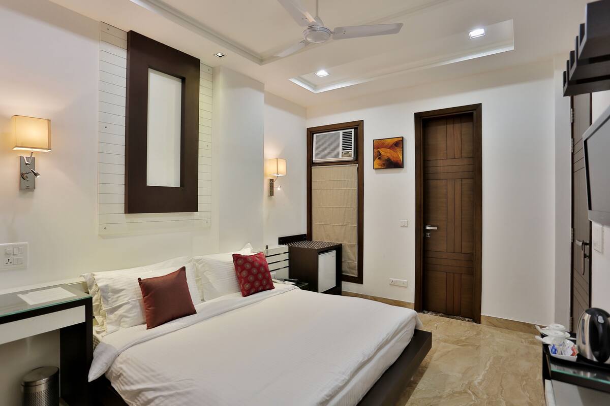 A hotel room with a bed, bedside table, lamp, ceiling fan, air conditioning unit, and a door.