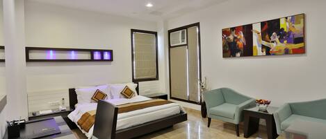 A modern hotel room with a bed, a desk, a chair, a coffee table, and a painting on the wall.