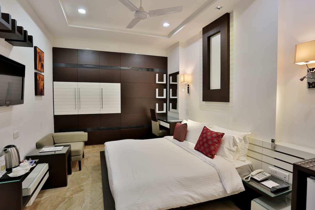 A modern hotel room with a large bed, a desk, a chair, a sofa, a TV, and a phone.