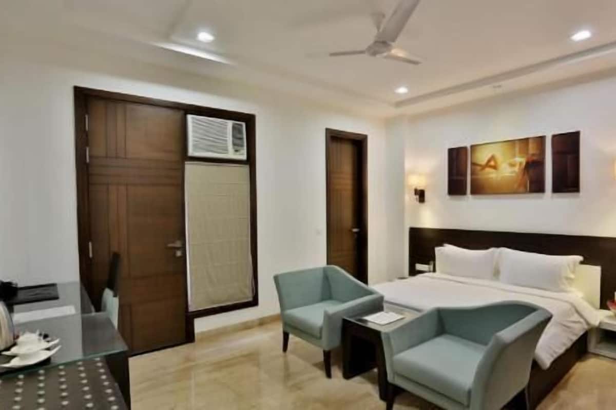A hotel room with a bed, two armchairs, a desk, and a ceiling fan.