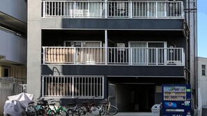 A multi-story building with balconies, a vending machine, and bicycles parked in front. - JL Residence Hotel (Osaka)