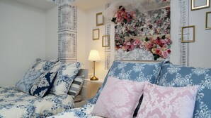 A bedroom with a bed, pillows, a nightstand, a lamp, and a floral wall decoration. - JL Residence Hotel (Osaka)
