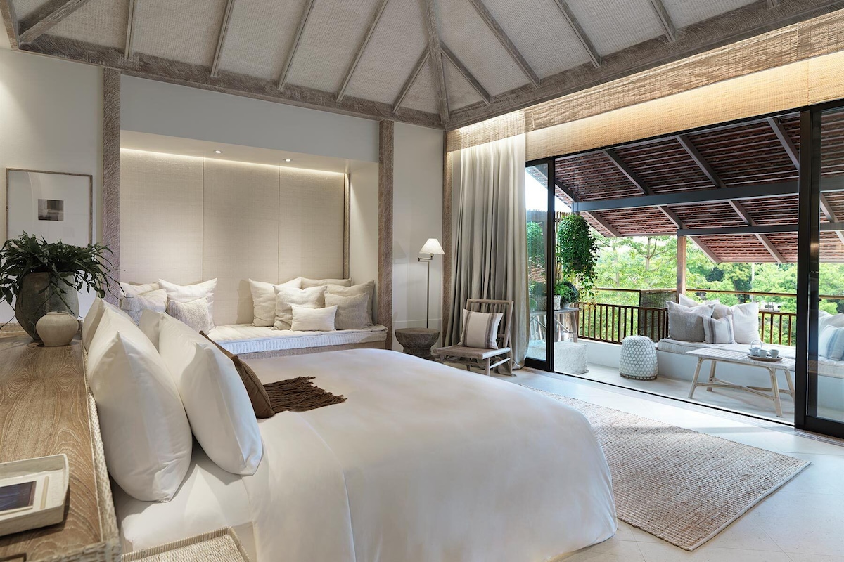 A spacious bedroom with a large bed, a seating area with a view of the outdoors, and a ceiling with exposed beams.
