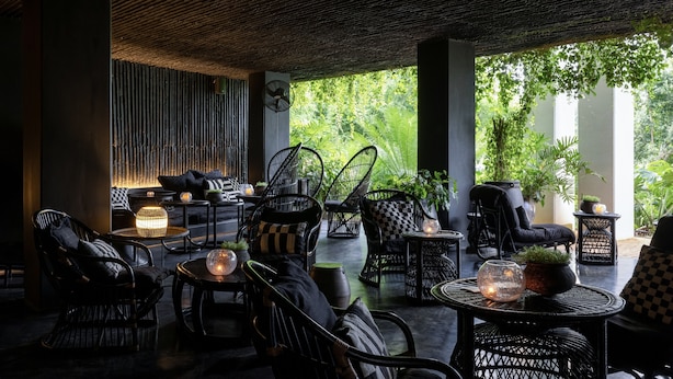 An outdoor seating area with wicker furniture, round tables, and potted plants. - Raya Heritage (Mae Rim)